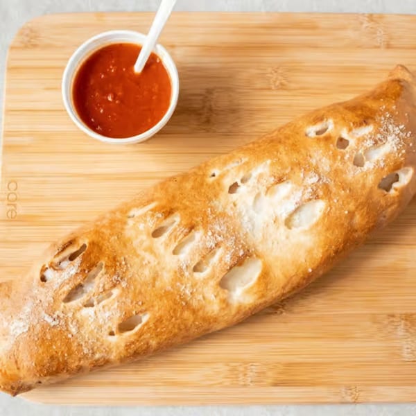 Golden-brown calzone with powdered sugar and a side of red marinara sauce on a wooden board.
