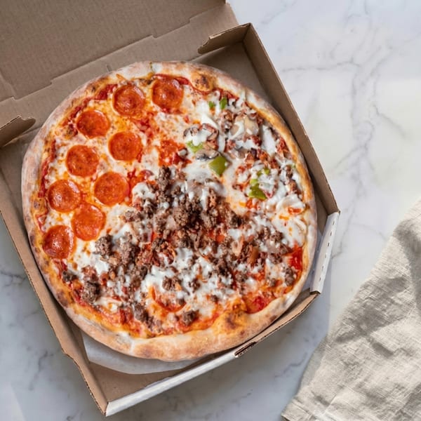 Half pepperoni, half meat and veggie pizza in a cardboard box on a marble surface.