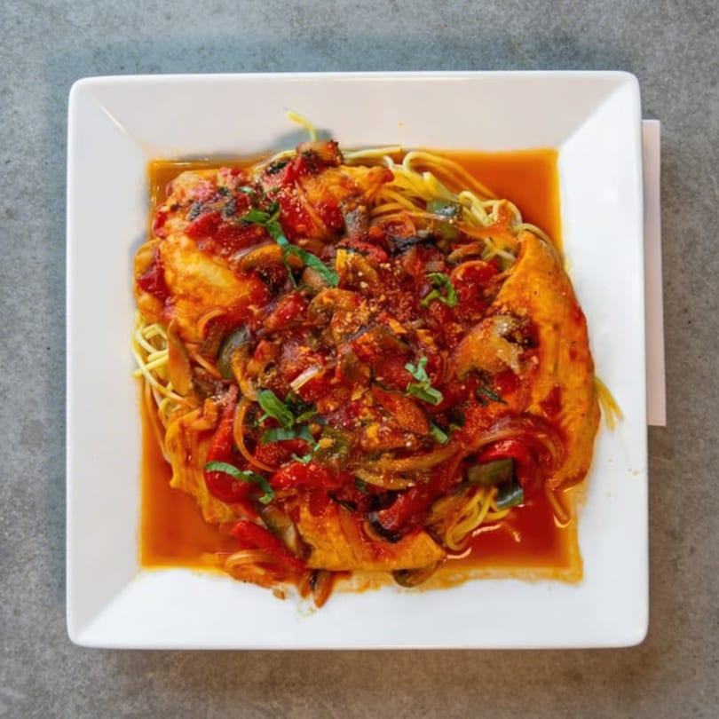 Chicken cacciatore with spaghetti, red sauce, peppers, mushrooms, and basil on a white plate.