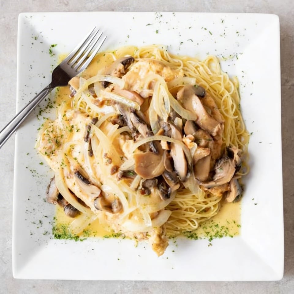 Angel hair pasta topped with chicken, mushrooms, and onions in a creamy sauce, with a fork.