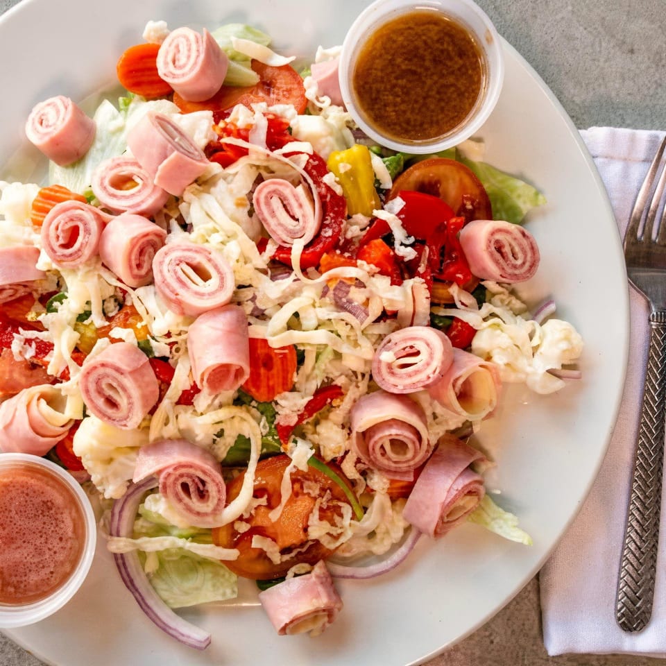 A Casa di Franco Pizzeria salad with ham rolls, cheese, lettuce, tomatoes, and two dressings.